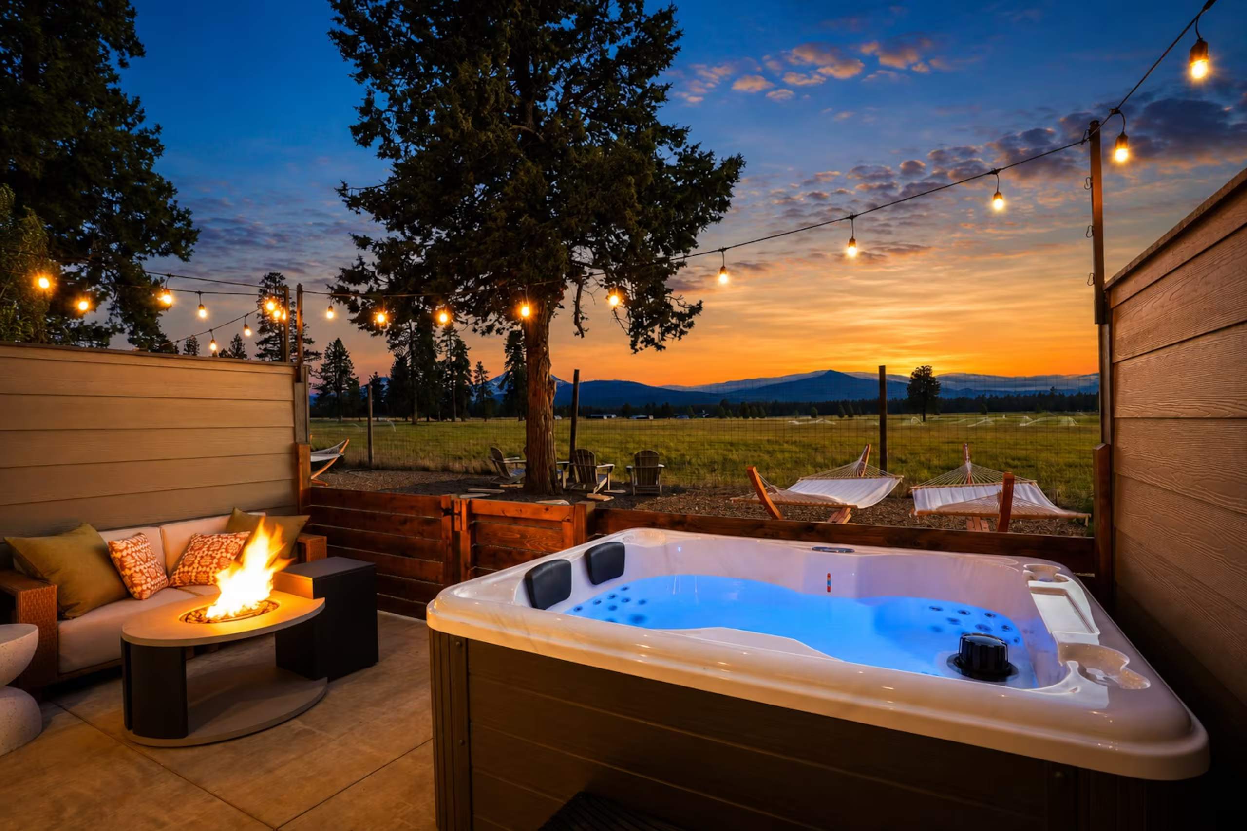 Private hot tub and fire table on a string-lit deck at sunset, with mountains on the horizon