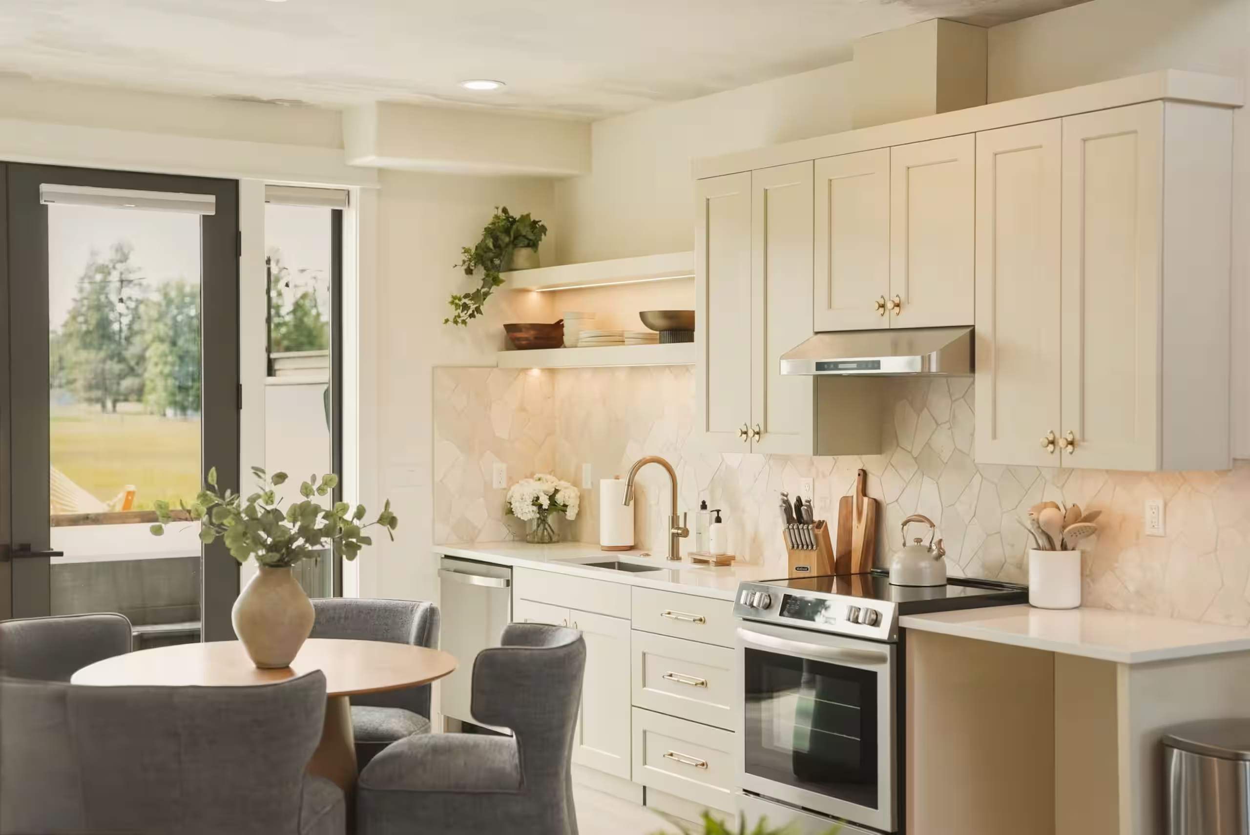 Bright kitchen with white shaker cabinets, a gold faucet and a round dining table by the window