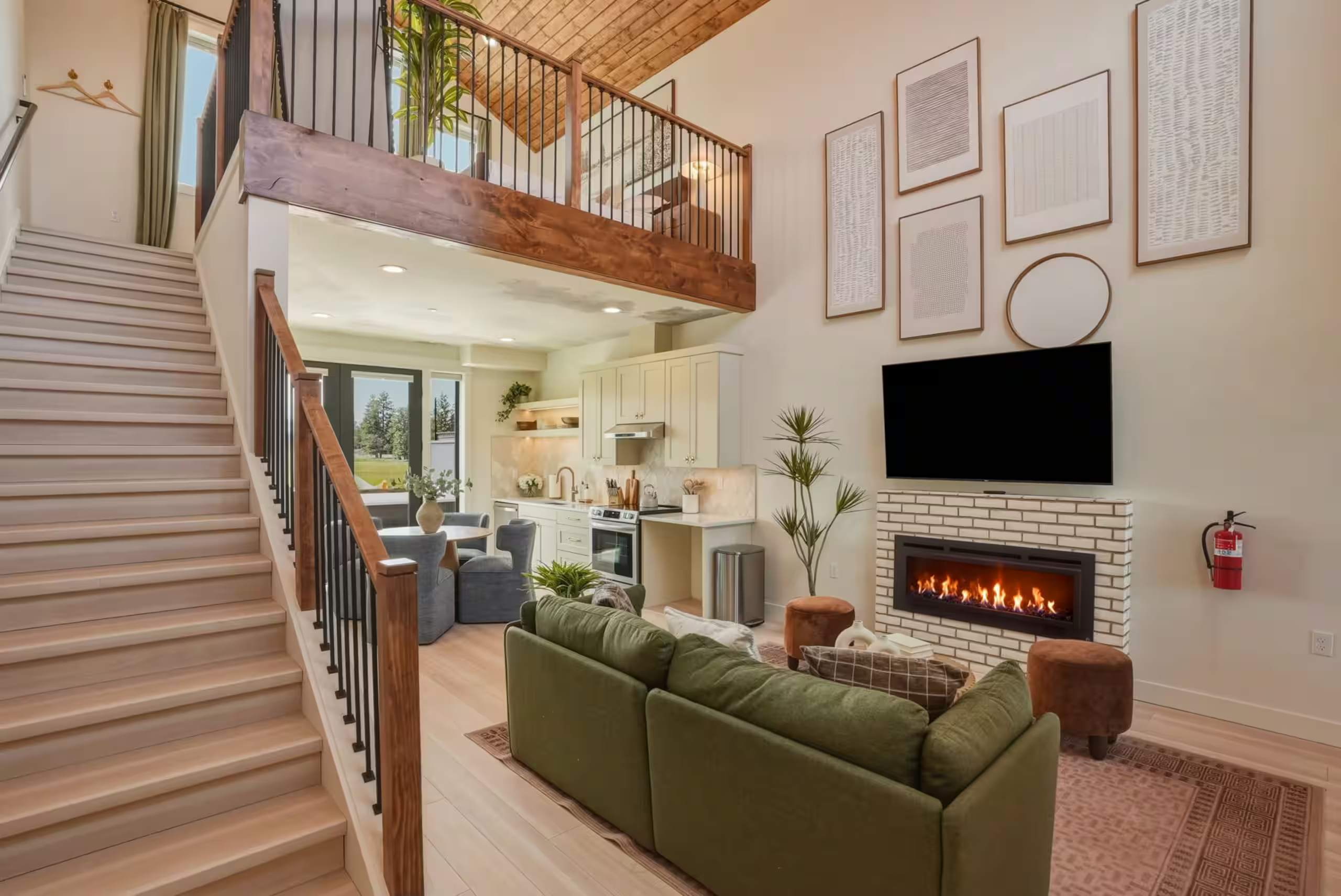 Open living room with a green sofa, linear gas fireplace and staircase up to a sunlit loft
