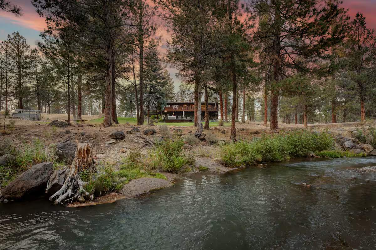 A clear creek winding past boulders and ponderosa pines under a pink evening sky