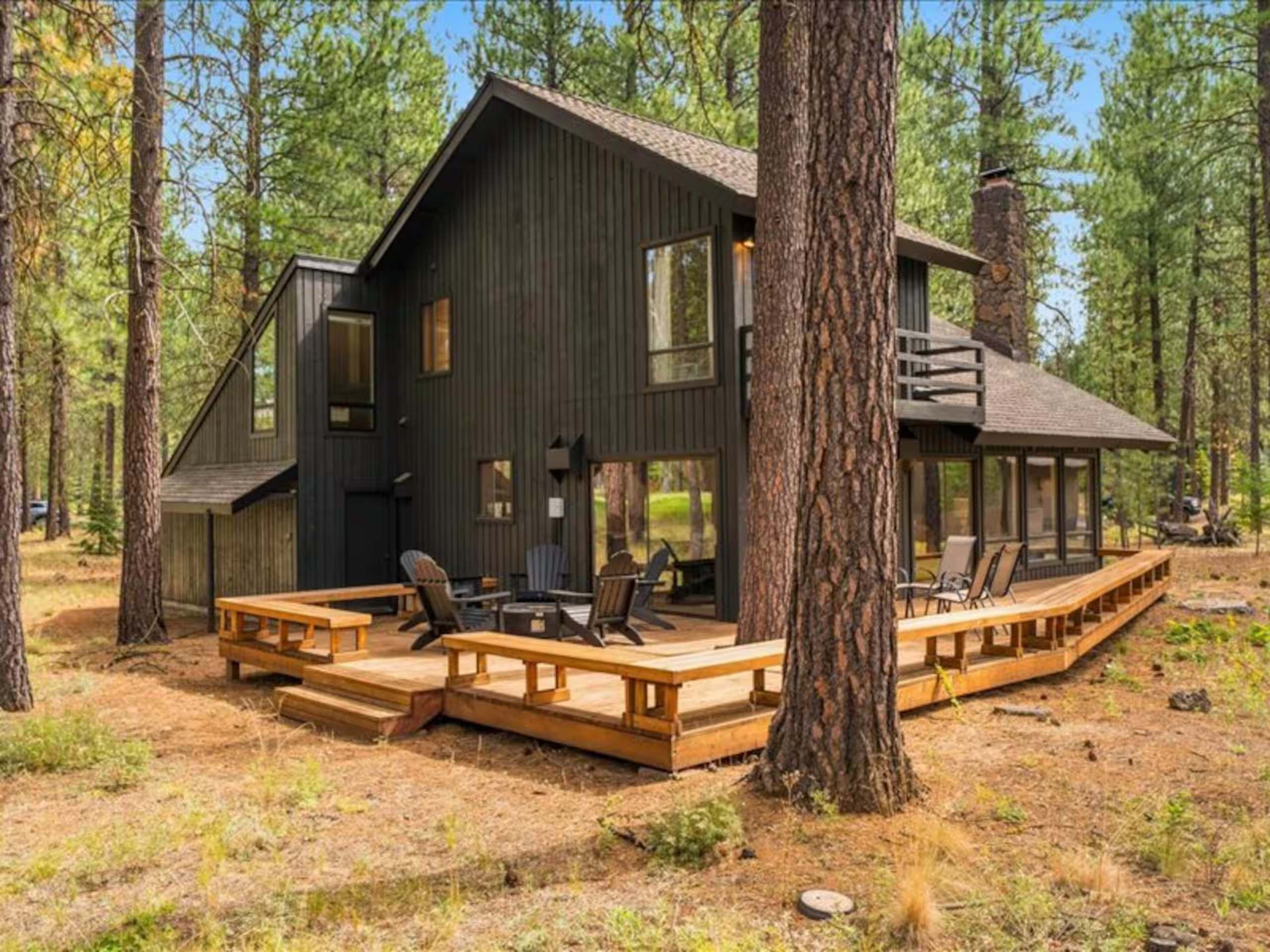 Black timber cabin with a wide cedar deck set among towering ponderosa pines